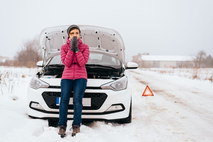 Woman standing by broken-down car in winter