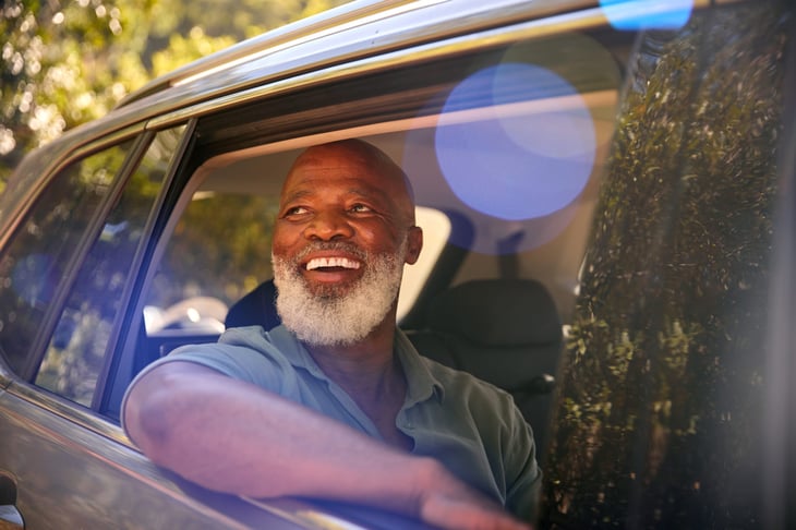 Smiling Senior Male Passenger Looking Out Of Back Seat Car Window