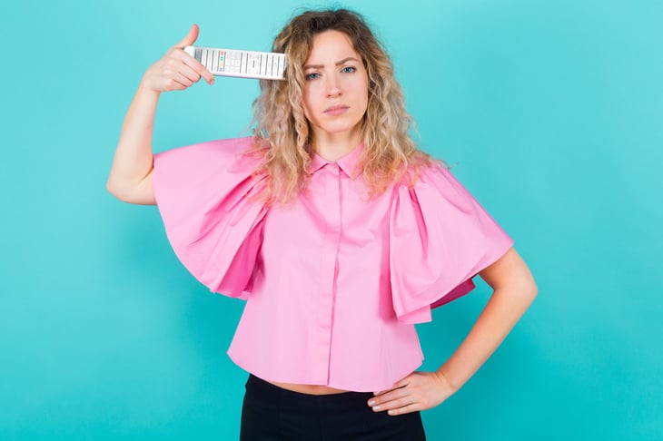 Annoyed or upset woman holding a remote control to her head because she wants to turn off the TV or change the television channel