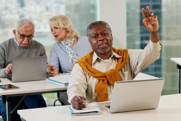 Senior in classroom raising hand to ask a question while looking at a laptop