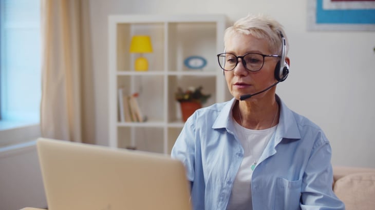 senior woman in a headset working at home office on a laptop.