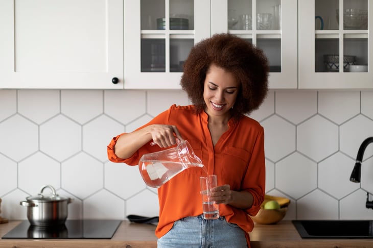 Smiling woman in the kitchen pouring a glass of water from a pitcher