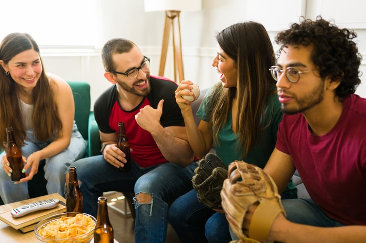Friends watching a baseball game on the tv while enjoying beer and snack