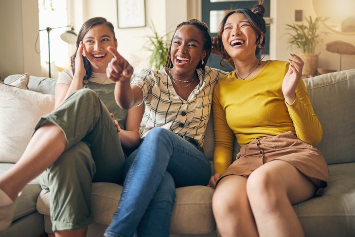 Three women laugh as they watch streaming live TV from a couch