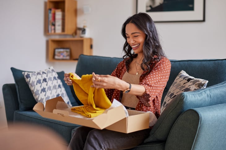 Smiling, happy woman at home opening a box from an online order. Shopping with free shipping.