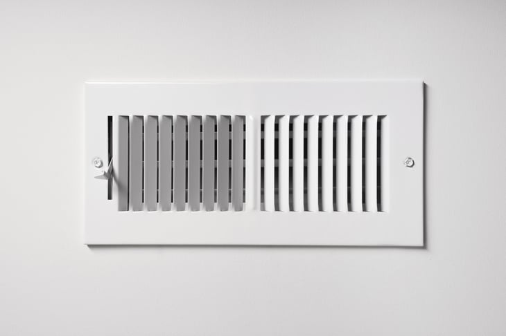 A heating/cooling vent register on the wall of a home, with open/close lever