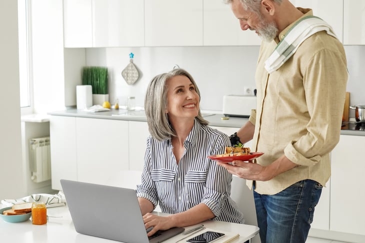 Retired husband bringing lunch to his working wife at home in the kitchen
