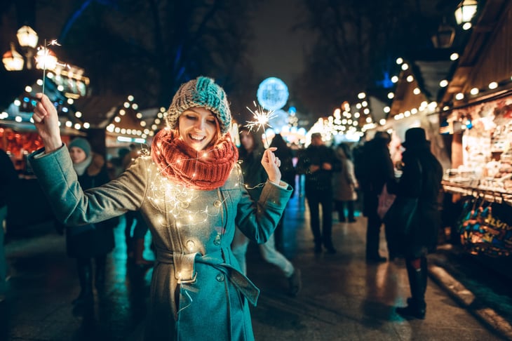 A woman holds sparklers at an outdoor holiday festival at night