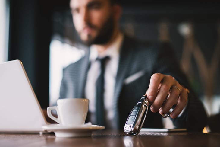 Businessman setting down his car keys as he looks at his laptop and drinks a coffee