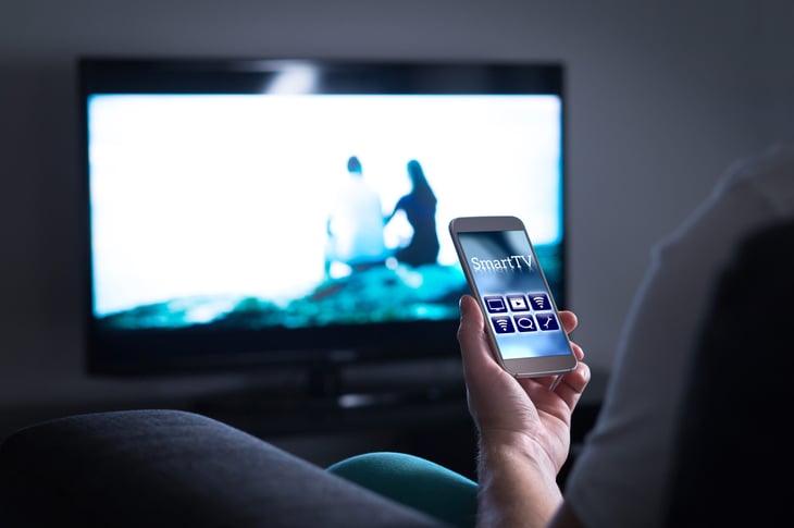 Man using a smartphone app as a TV remote control