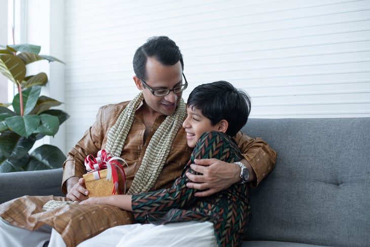 Father in traditional Indian attire hugging and giving a gift to his son
