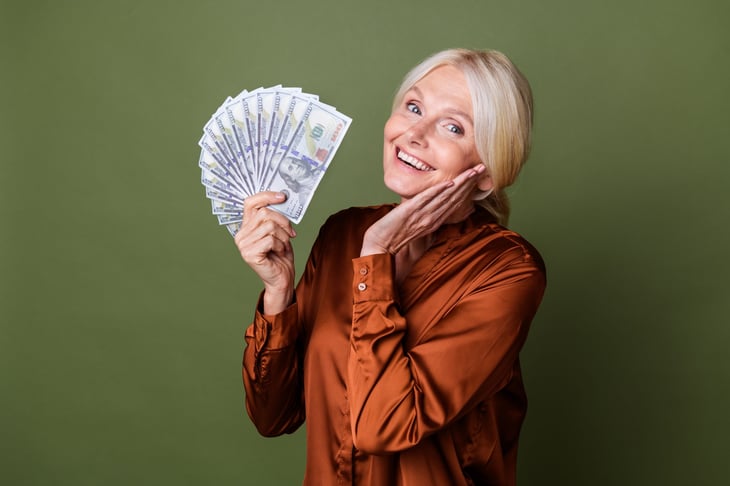 Happy grateful senior woman holding over a thousand dollars in cash and smiling