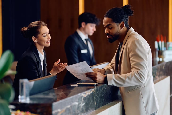 Smiling hotel manager assisting a guest with a bill at the reception desk.