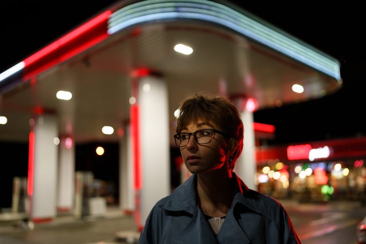 Woman wearing glasses at a gas station at night looking cautious