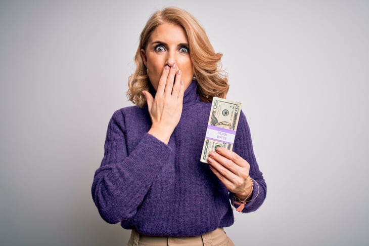 Shocked middle-aged woman holding a stack of cash