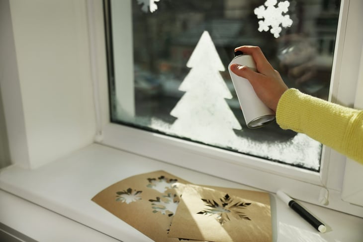 Woman using snow spray for decorating window at home