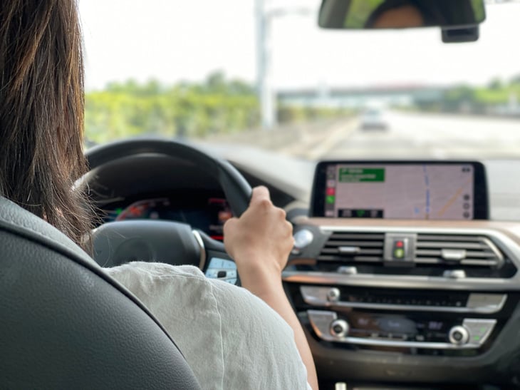 Woman behind steering wheel of a car looking at the road with a passenger view of the dashboard and driving route on GPS
