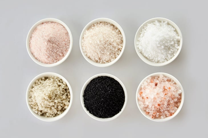 Six assorted gourmet salts in bowls with black Hawaiian lava salt, Indus salt, Fleur de sel, rock salt and sea salt