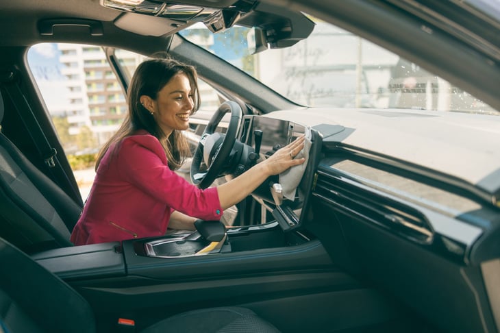 Woman smiles as she wipes down the dashboard of her new car.