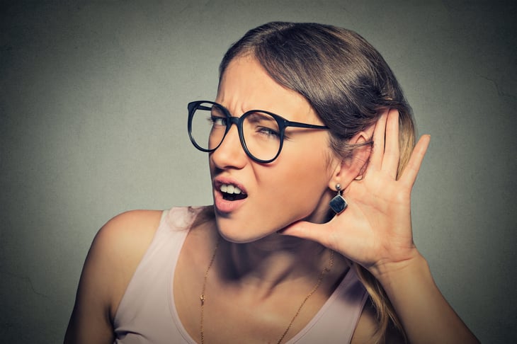 Woman cupping her ear trying to eavesdrop or having difficulty hearing and saying "Huh?" or in disbelief