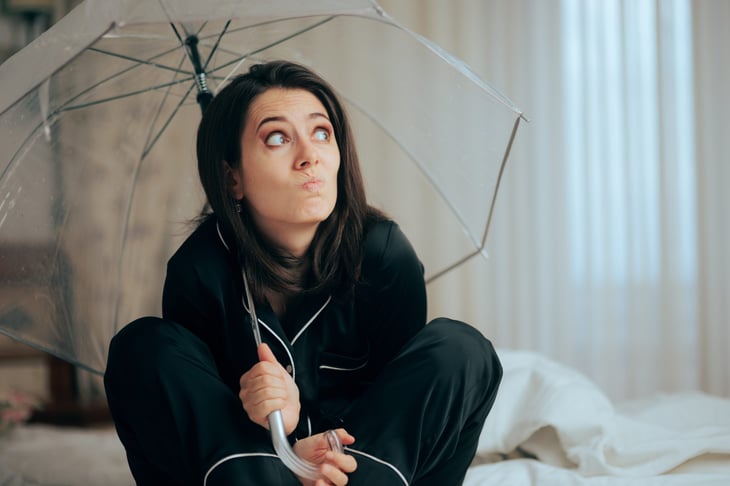 Worried woman holding an umbrella and clutching the handle in worry or fear because she does not have insurance