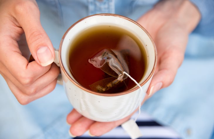 person holding cup of tea with tea bag inside