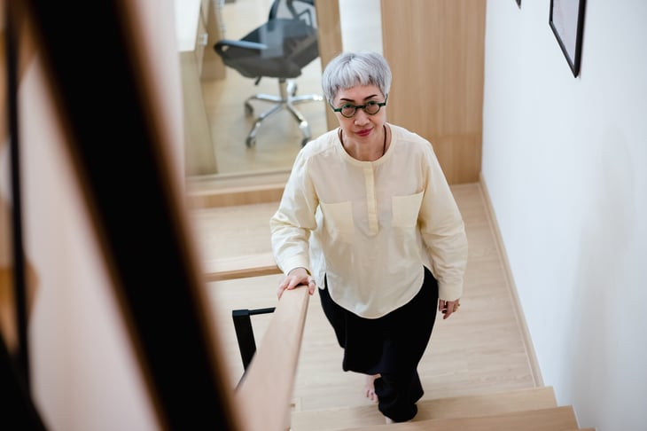 Senior woman with glasses walking up a staircase and taking the office stairs instead of elevator for exercise