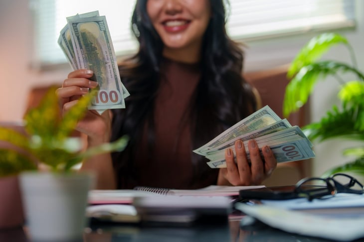 Smiling woman counting a thick stack of American one hundred dollar bills, enjoying financial success