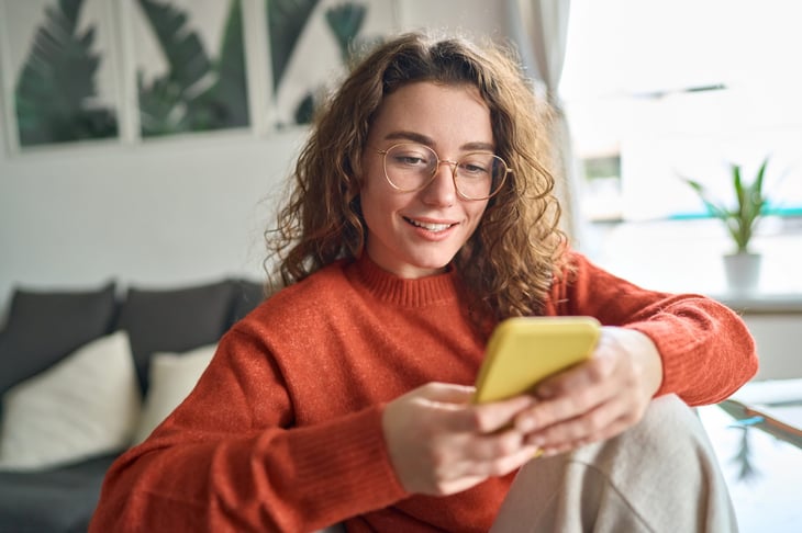 Smiling woman looking at phone happily and thinking about typing a response