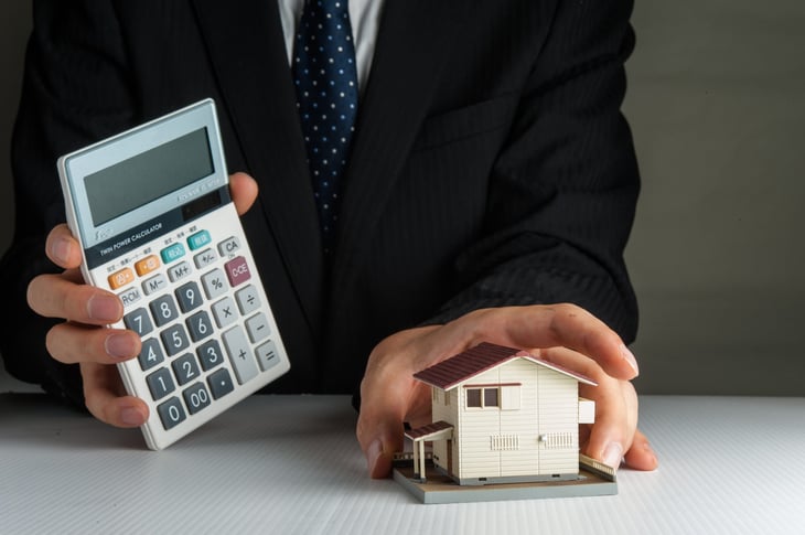 Man in a suit holding a calculator and model of a home.