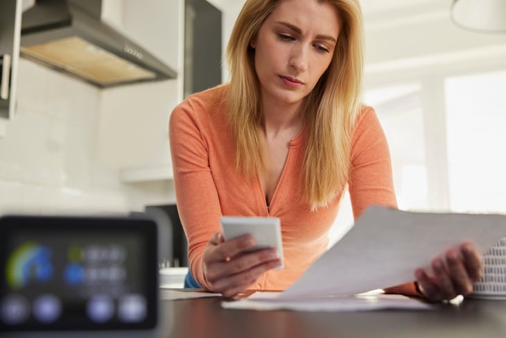 Woman looking thoughtful at her phone and a bill