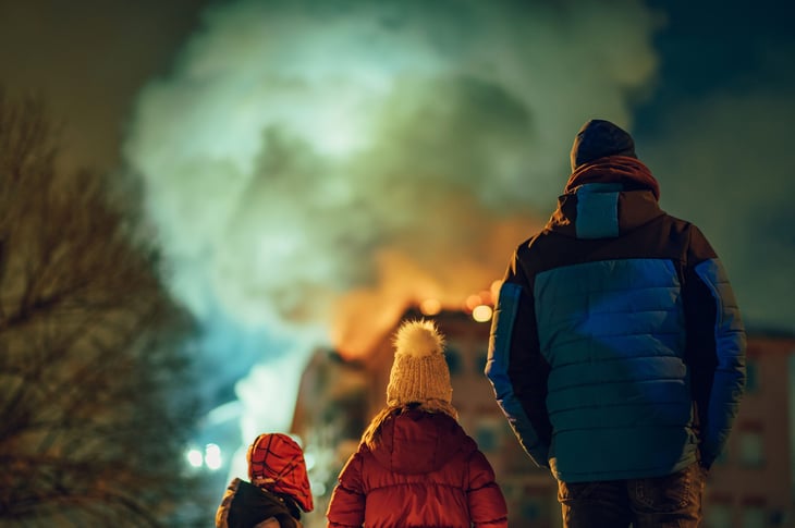 Family standing outside in the cold in winter jackets while a house burns down
