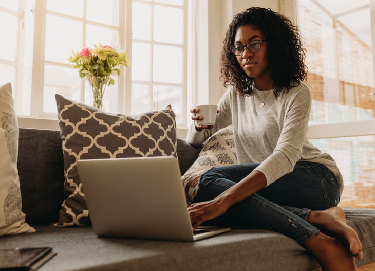Woman using a laptop on her sofa and drinking coffee
