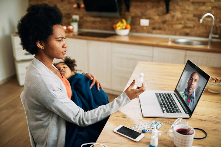 mother using laptop and having online appointment with a doctor while holding her sick child in her lap at home