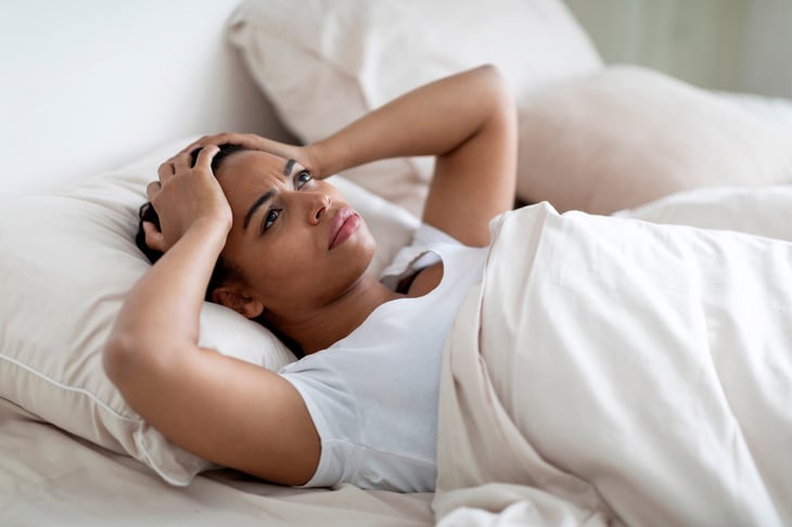 Worried woman holding her head in bed