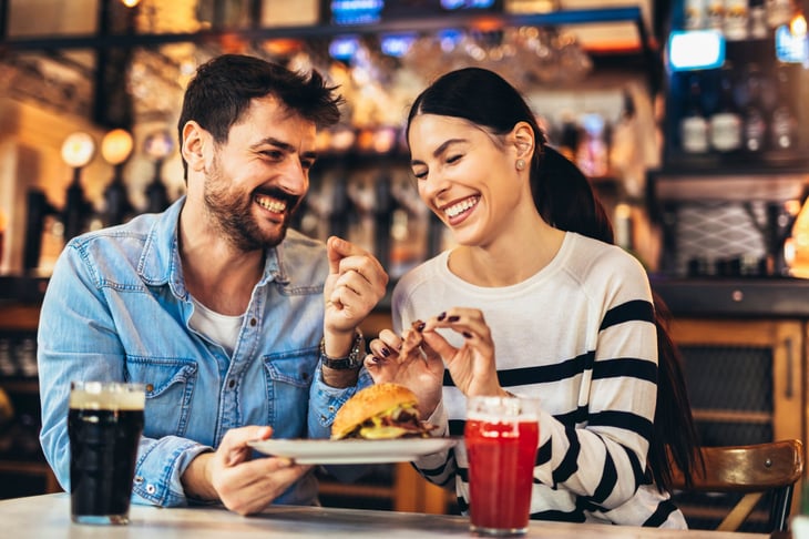 Happy couple on a date eating a cheeseburger at a restaurant