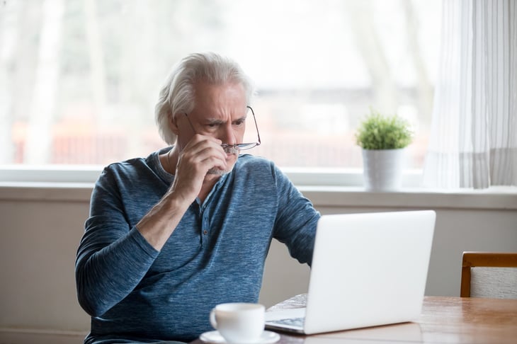 Shocked, frustrated senior man taking off glasses to look at laptop