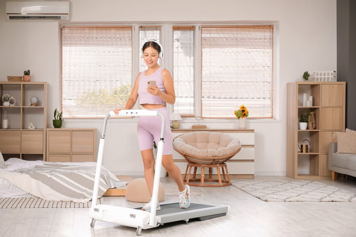 Woman with headphones and phone training on treadmill in a bedroom