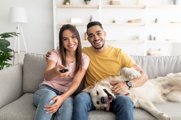 Couple sitting on couch with their dog, watching TV at home