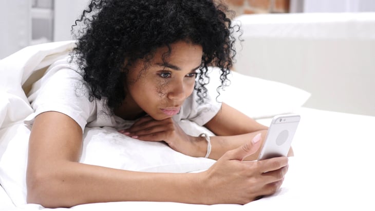 Woman laying in bed and scrolling on her phone.