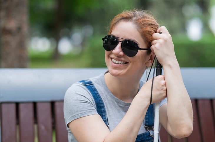 Smiling woman who is blind wearing dark sunglasses and carrying a mobility cane or walking stick