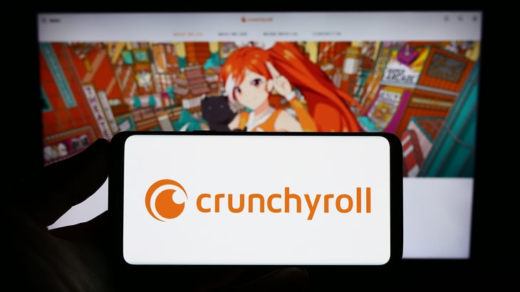 Person holding smartphone with logo of US entertainment company Crunchyroll LLC on screen in front of website