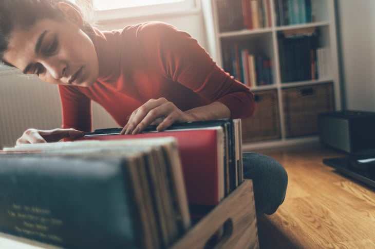 Woman looking through a crate of vinyl records in a home.