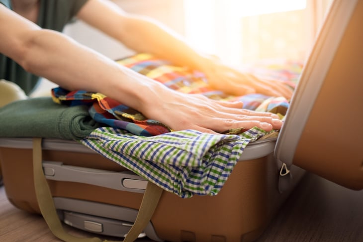 Man or woman packing suitcase full of clothes or carry-on luggage bag