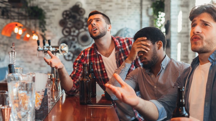Upset friends watching football half time show and drinking beer in sports bar