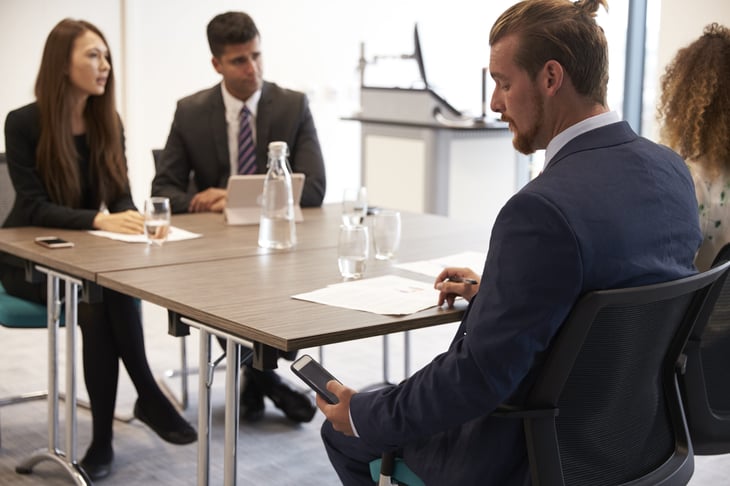 Man looking at his phone under the desk during a business meeting.