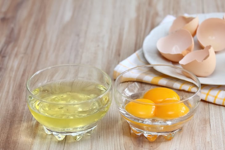 Egg whites separated from egg yolks for cooking with cracked eggshells in the background