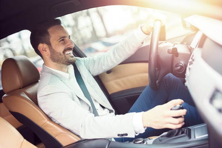 A businessman smiles while driving his car on a sunny day.