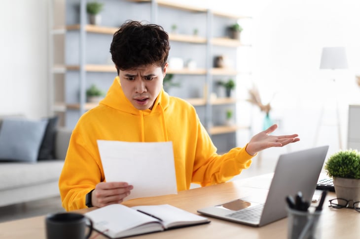 Frustrated man working at laptop and angry at paperwork