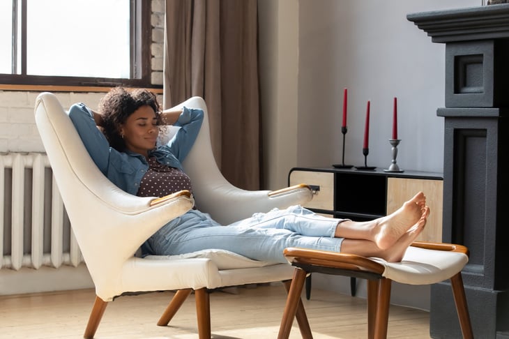 Relaxed homeowner smiling woman lounging in a chair in her living room at home with her feet up